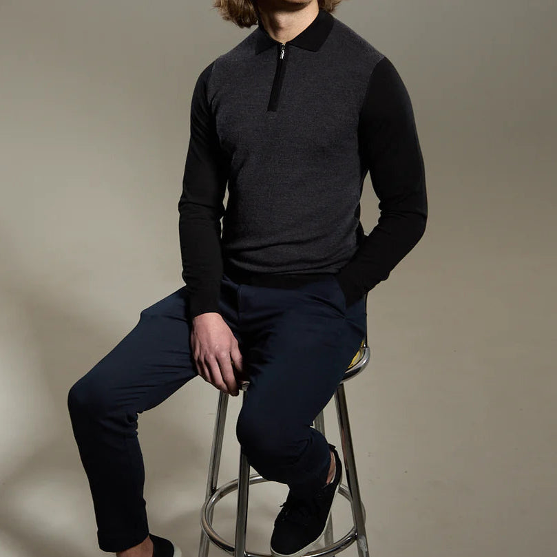 A person sitting on a stool wearing a black micro stitched knitted polo shirt and dark pants.